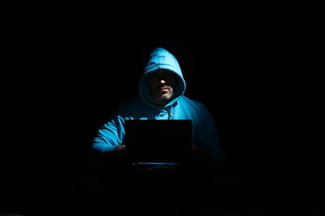 Hooded figure at laptop representing cybersecurity threats driving AI security market vendor growth