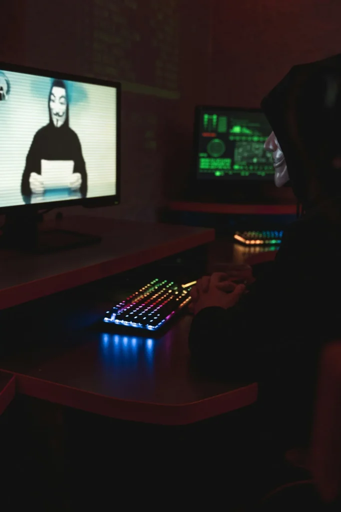 Hacker workstation with Anonymous mask on screen representing AI-powered security threats