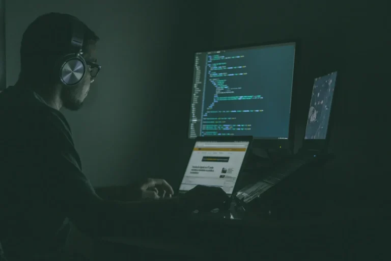 Cybersecurity professional wearing headphones working at multi-monitor setup with code for AI security course training