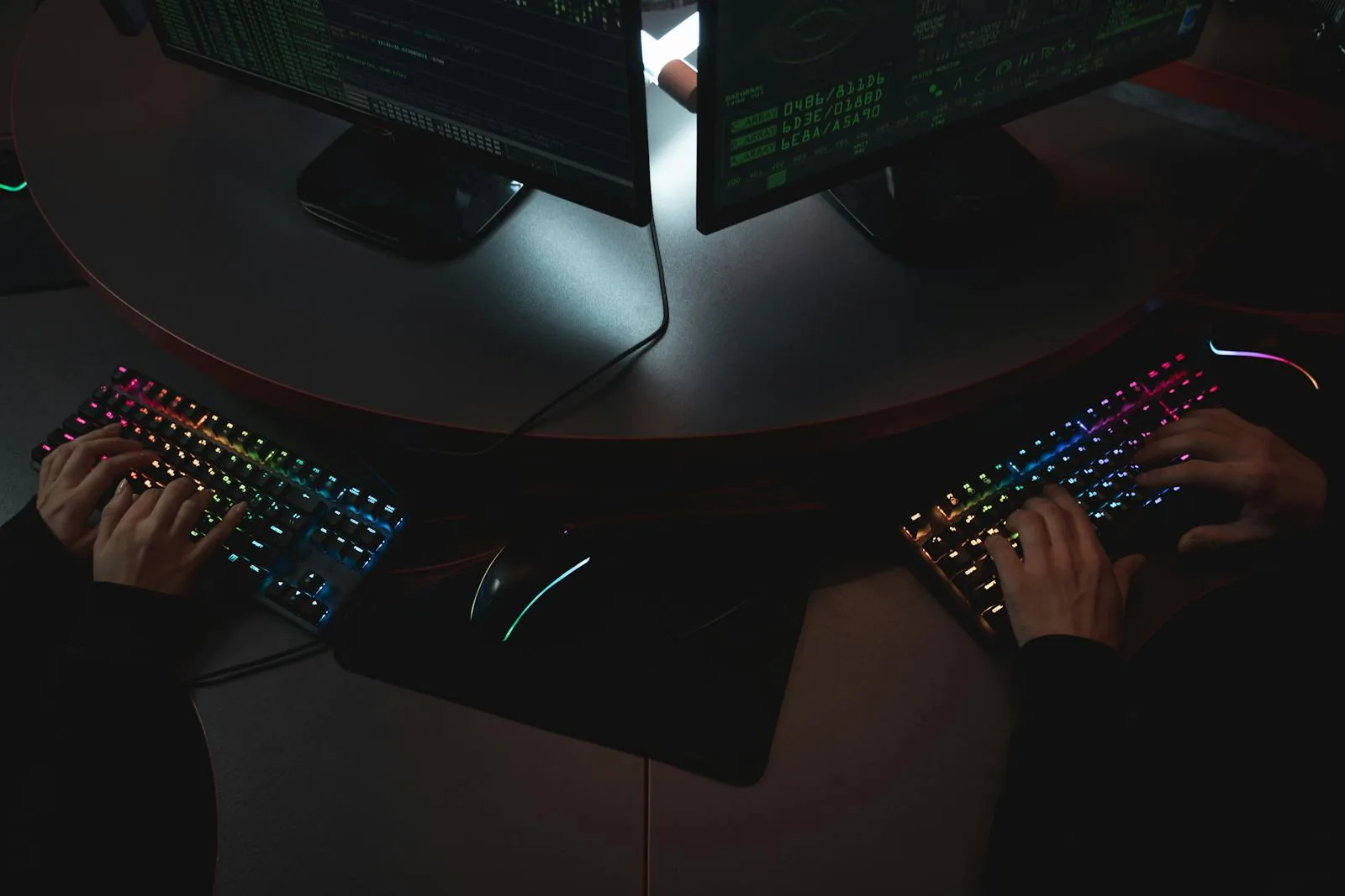 Two cybersecurity practitioners typing on RGB keyboards with security code on monitors representing online AI cybersecurity course learning