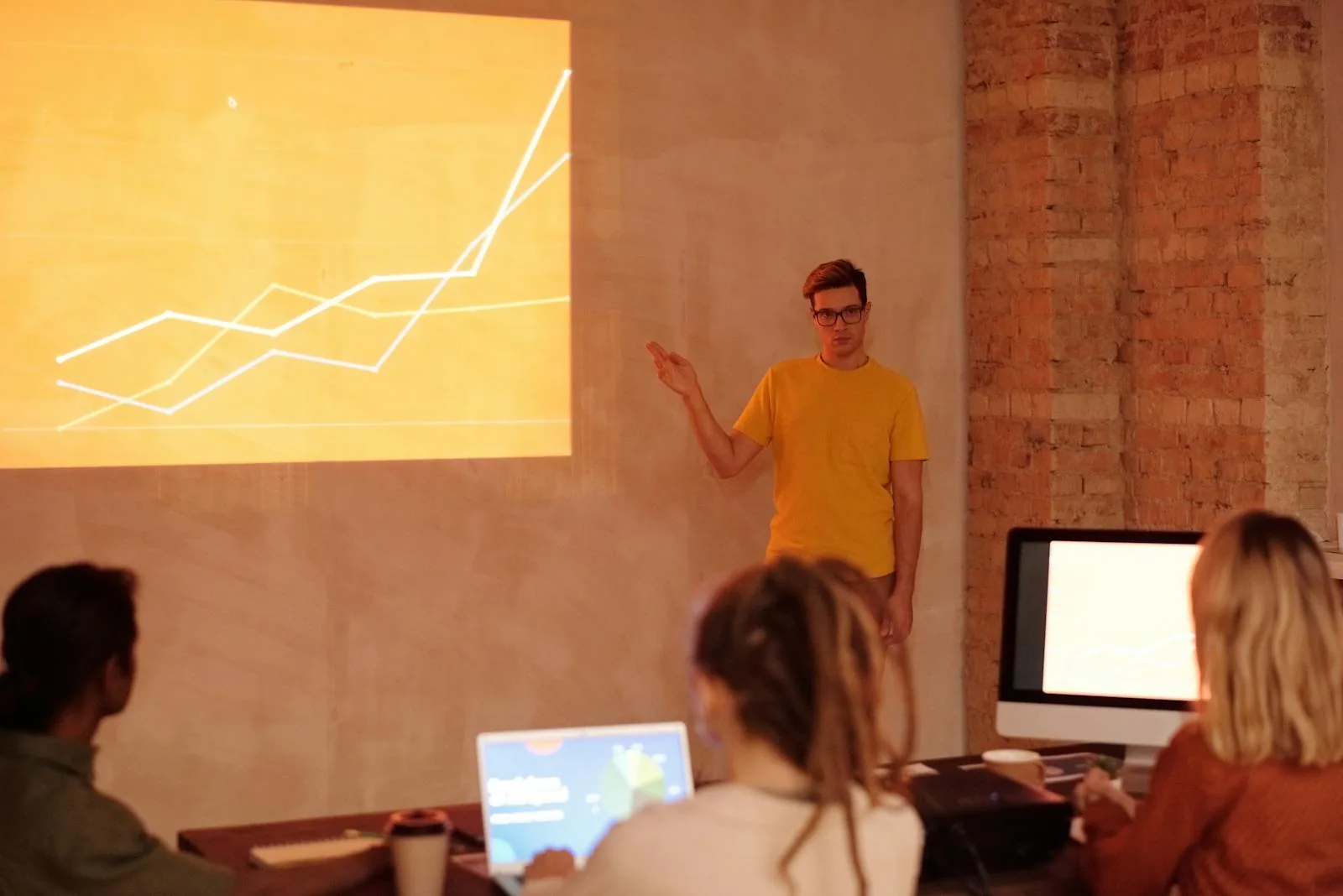 Presenter standing next to projected data analysis line chart with audience listening in modern workshop setting