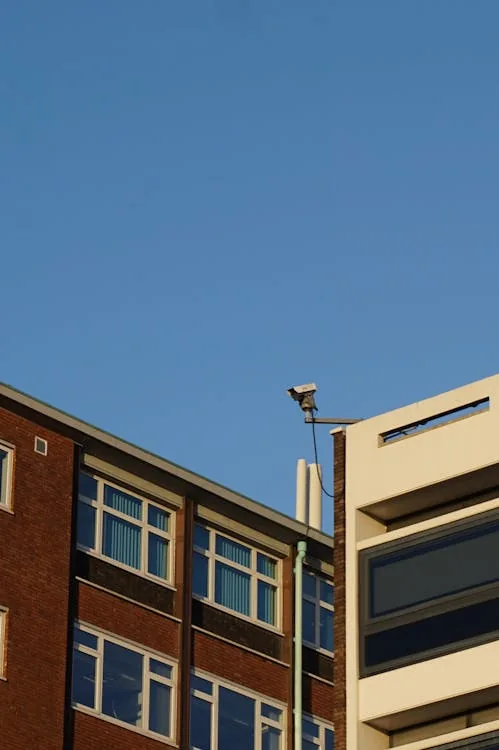 Security camera mounted on university building corner against clear blue sky representing AI-powered school security surveillance systems