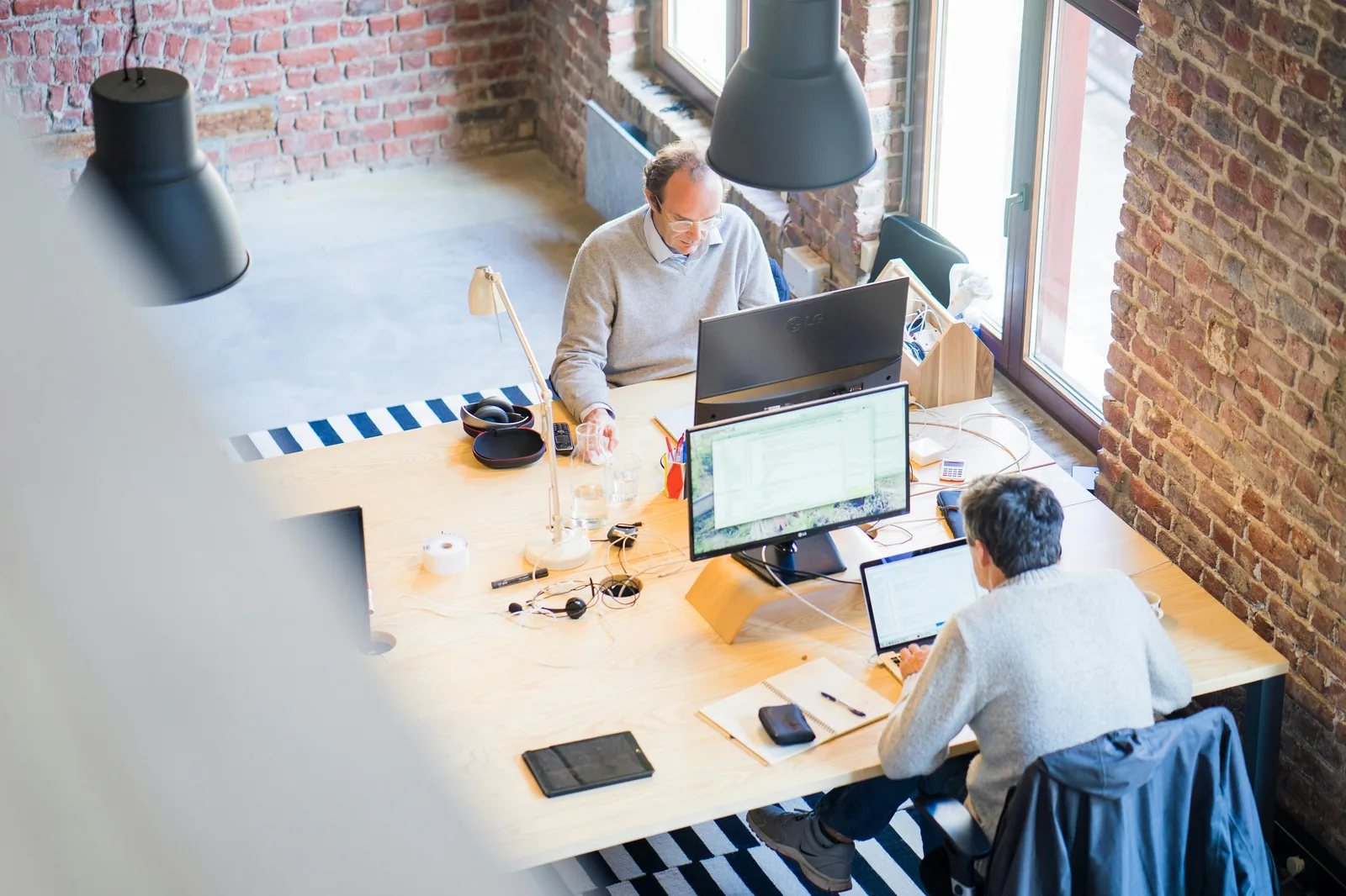 Overhead view of two technology professionals working at computers in modern startup office