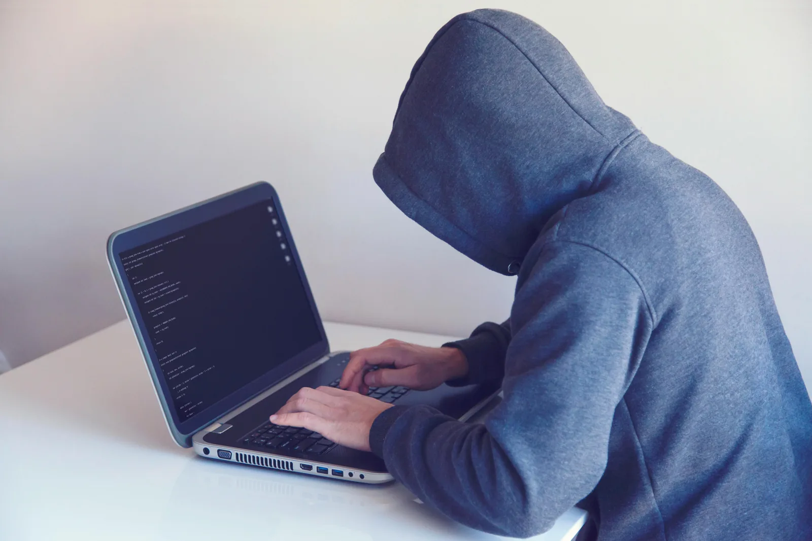 Anonymous hooded figure accessing laptop representing AI system threats and shadow AI