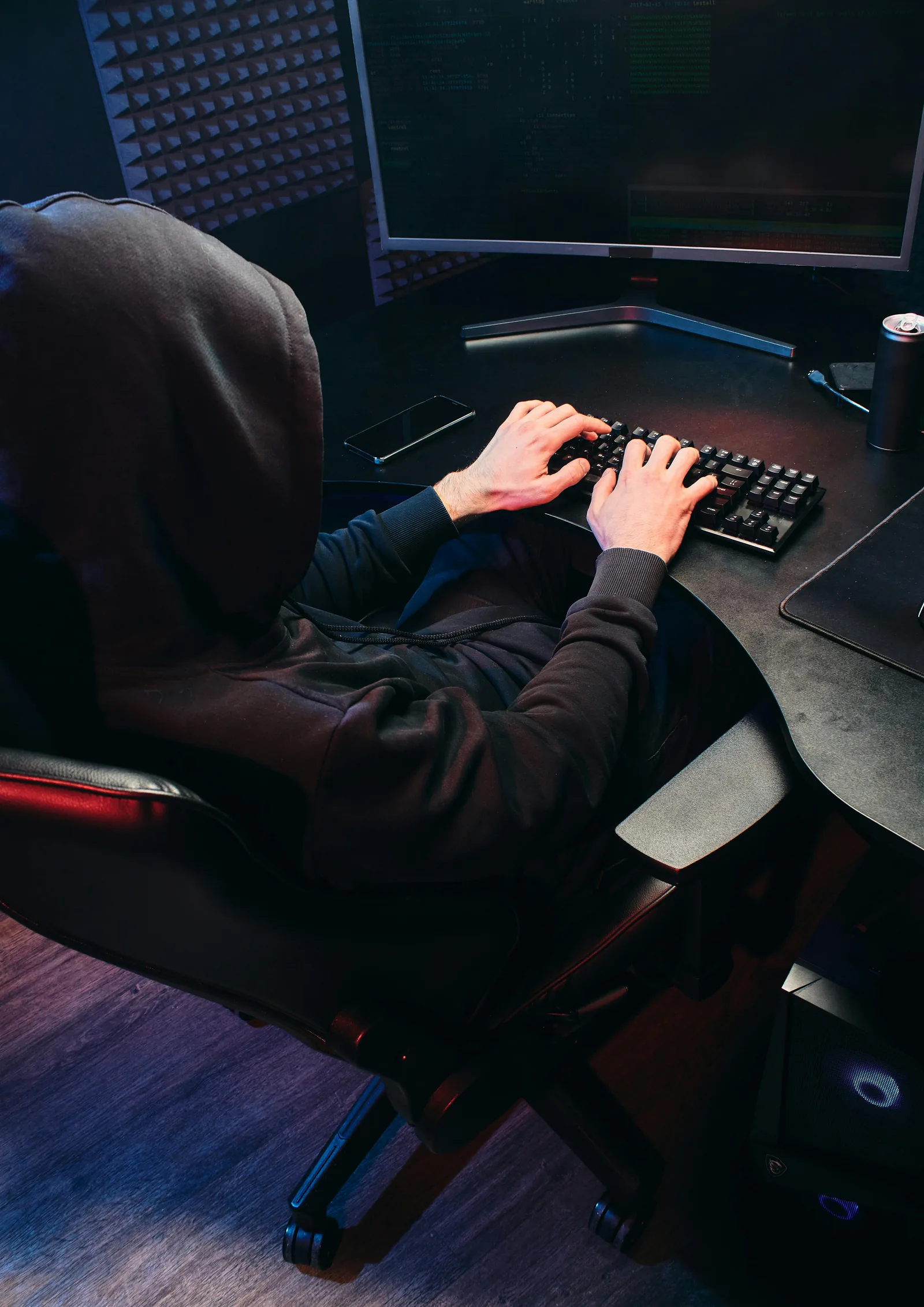 Hooded cybersecurity threat actor typing at keyboard in dark room
