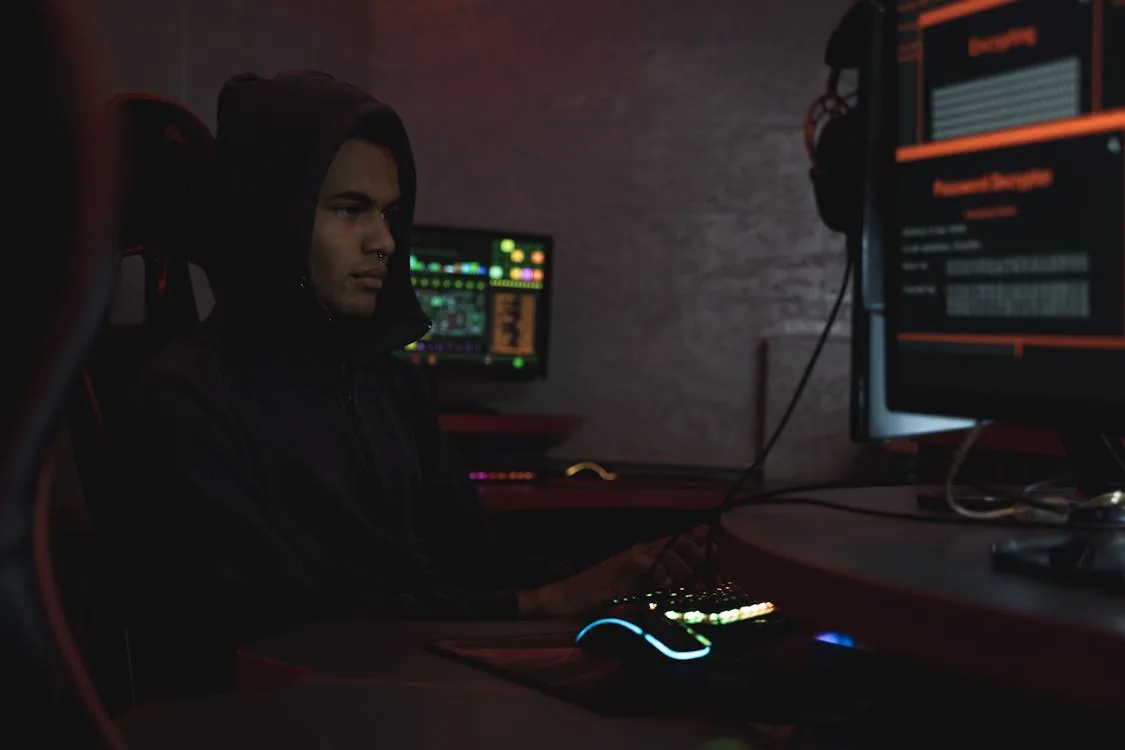 Cybercriminal in dark room running AI-powered attack tools including phishing and exploitation automation
