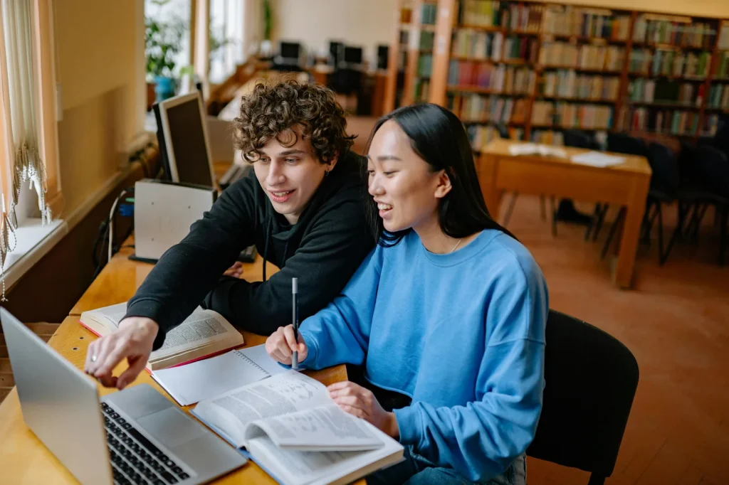 Students collaborating with laptop and books in bright university library representing cyber security and intelligence studies programs academic curriculum