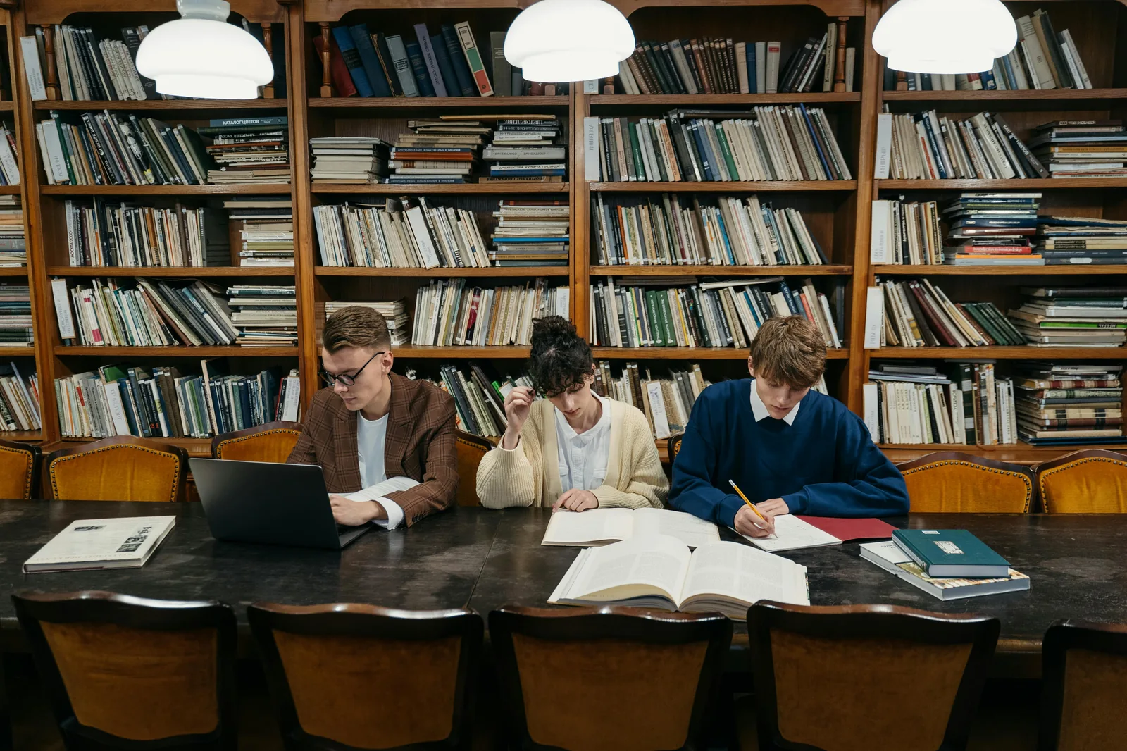 University students studying in bright library with books and laptop representing cyber security and intelligence studies degree programs UK US NCSC certified
