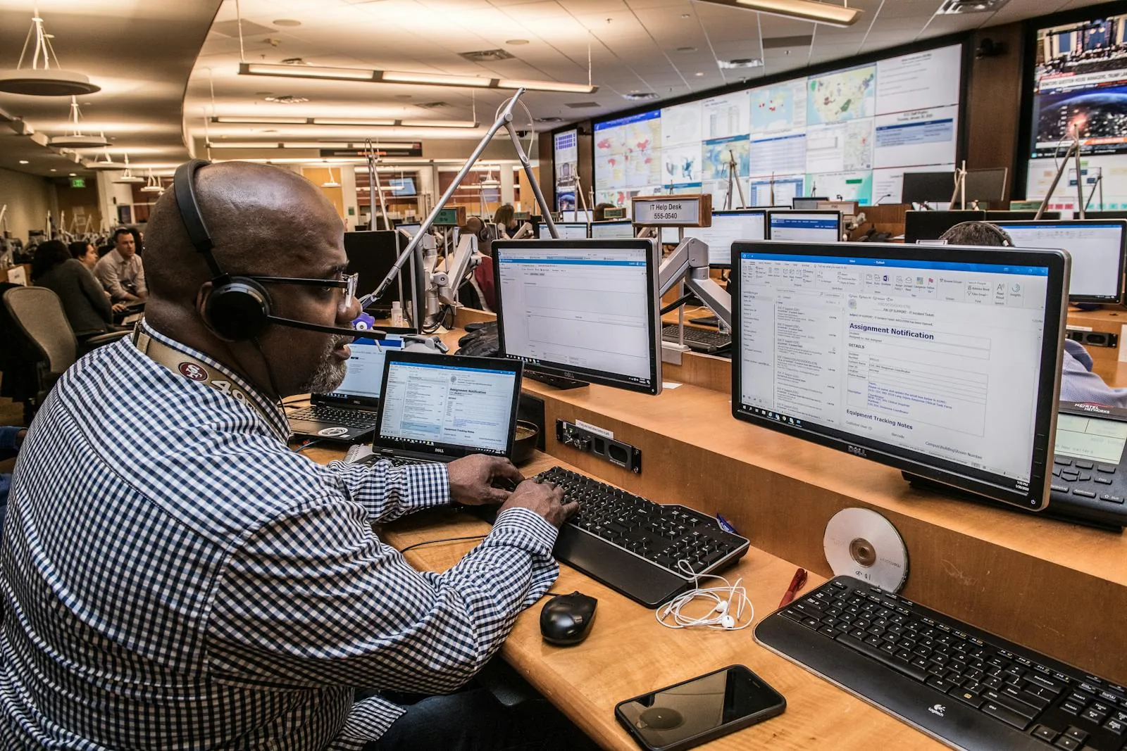 Security operations center analyst with headset working at multi-monitor desk with large wall displays for threat intelligence integration