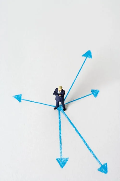 Miniature businessman at blue arrow crossroads representing the cyber security vs artificial intelligence career decision