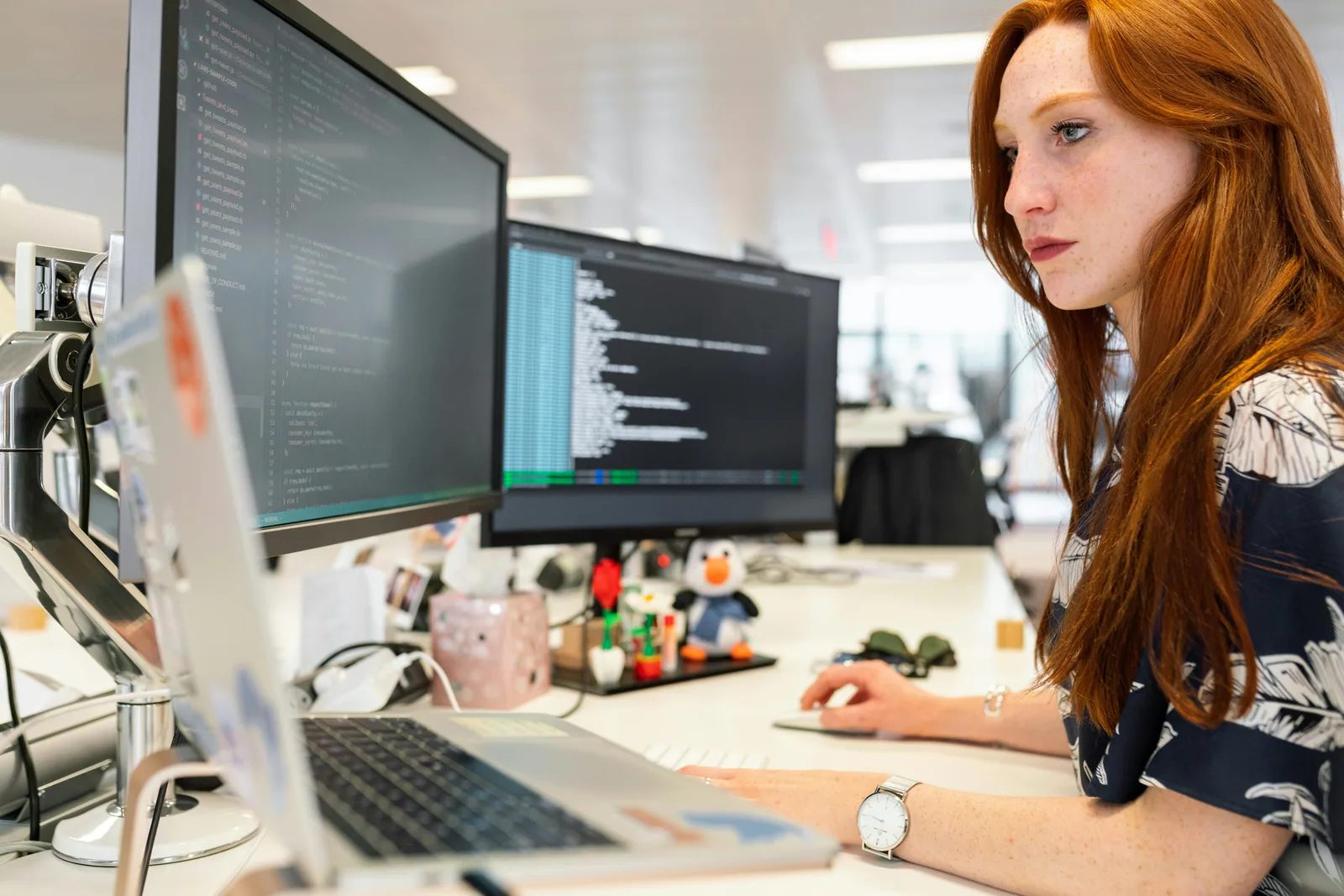 Cybersecurity professional working at dual monitors in bright open office representing intelligence and cyber security studies careers salary certifications job outlook