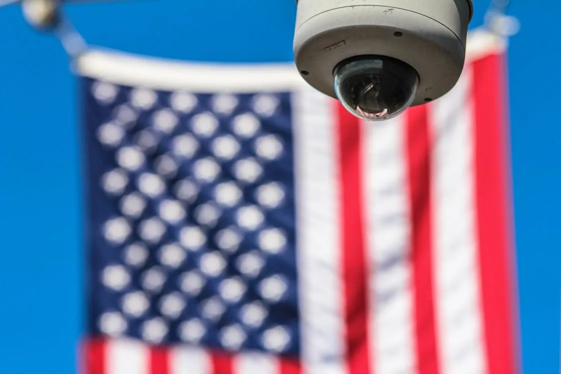 Dome surveillance camera in front of American flag representing US national security intelligence services and their collection missions