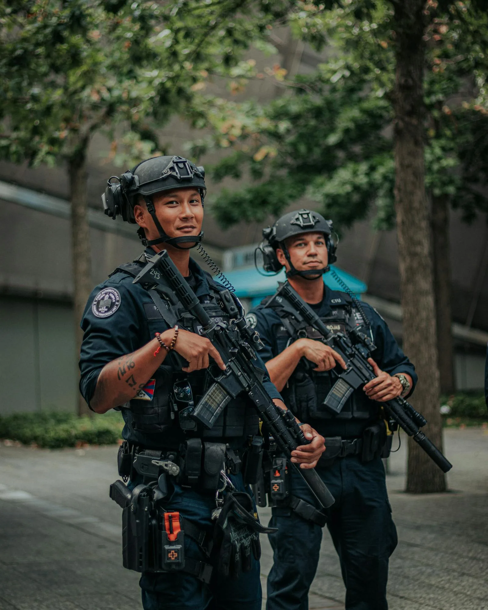 Two armed law enforcement officers in tactical gear with rifles and helmets patrolling urban area representing security career paths