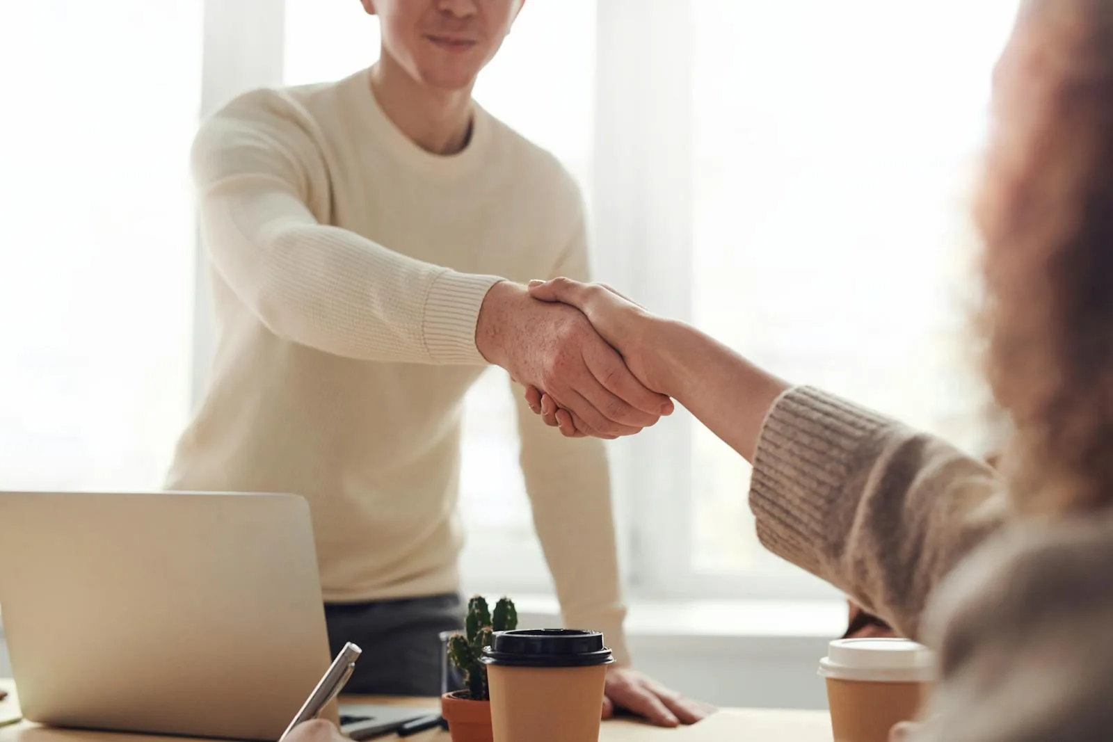 Two professionals shaking hands across a desk in bright office setting representing career placement and employer connections in intelligence studies