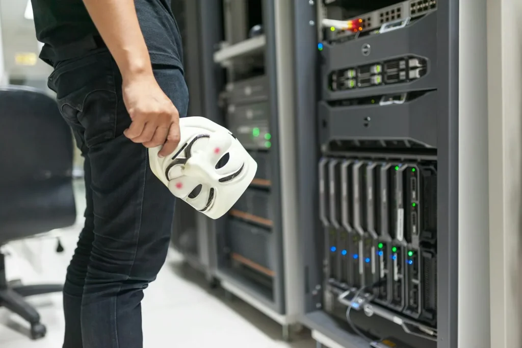 Anonymous mask held near server rack representing adversarial threats that Robust Intelligence AI security platform defends against