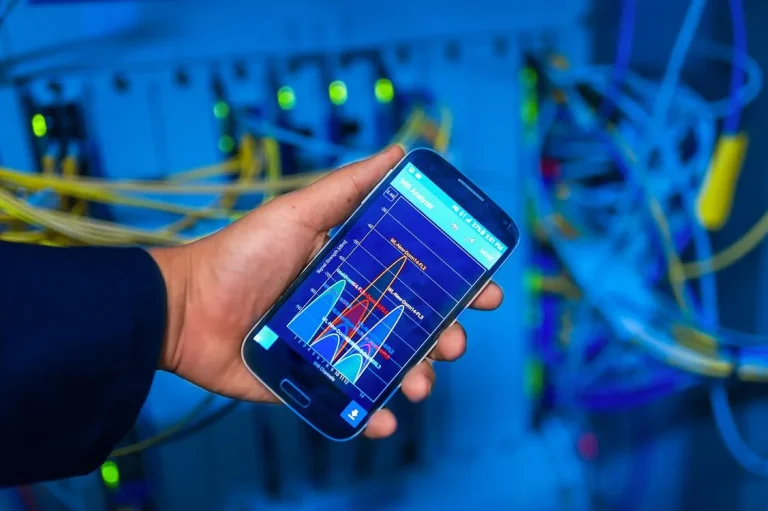 IT professional holding smartphone showing network analysis data in blue-lit server room representing security intelligence platform monitoring